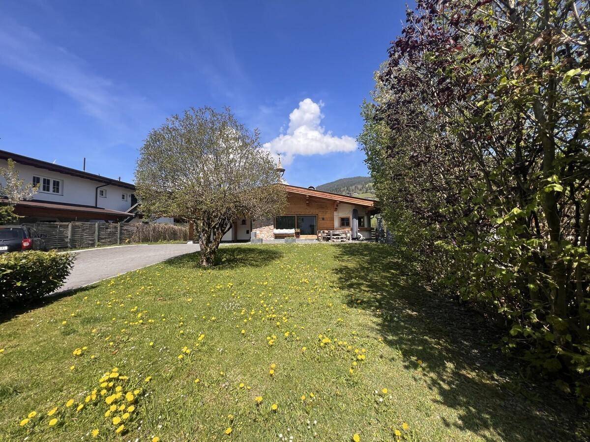 Gepflegter Garten mit grüner Wiese und blühenden Blumen vor dem traditionellen Holzhaus.