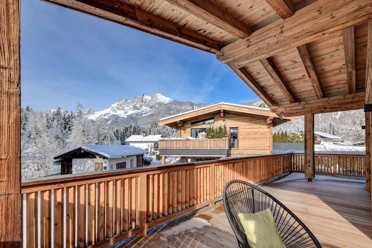 Geräumiger Holzbalkon mit Blick auf die schneebedeckten Berge und umliegende Häuser.