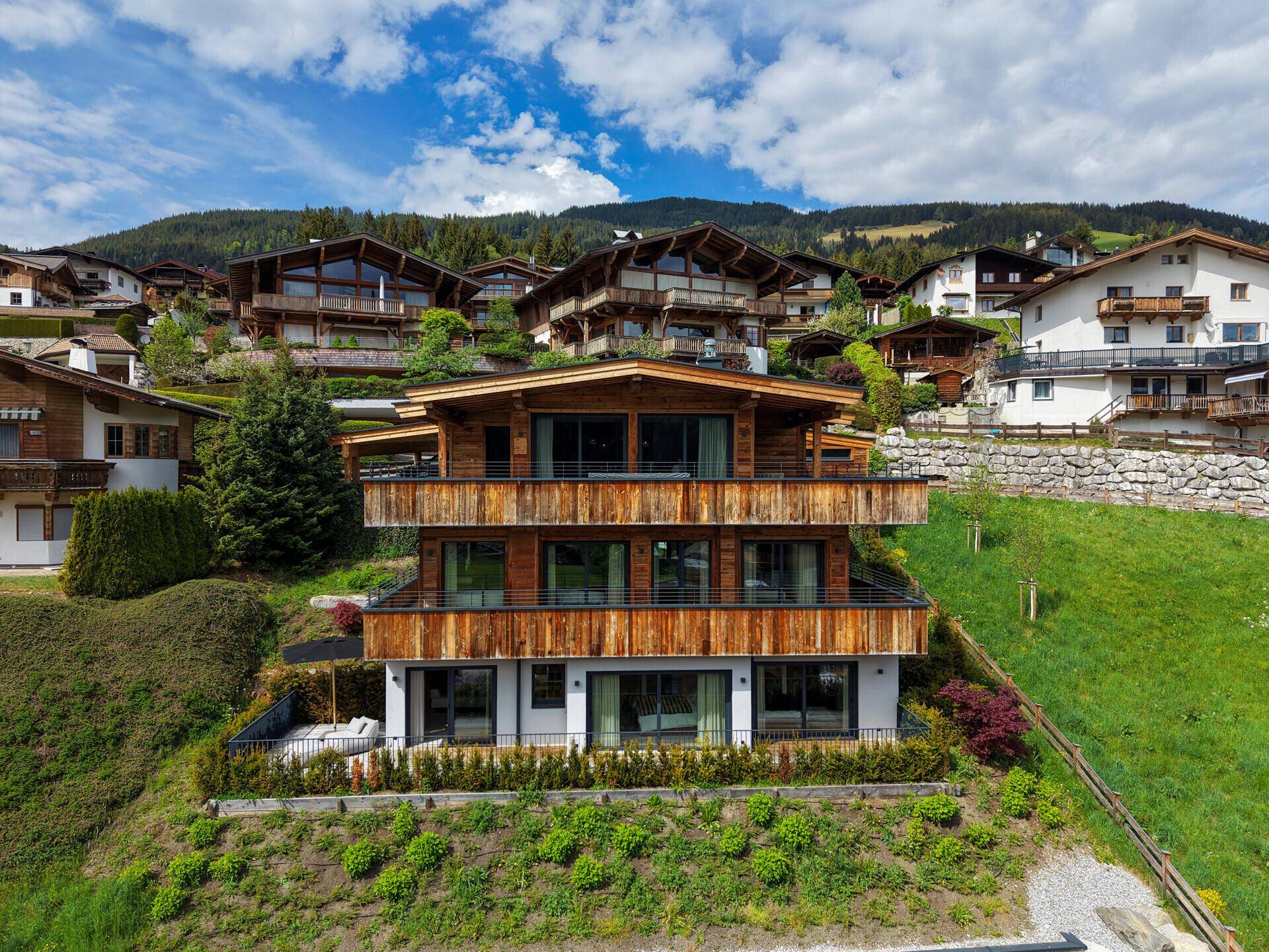 Modernes Chalet mit Holzfassade und mehreren Balkonen, eingebettet in eine grüne Hanglage.