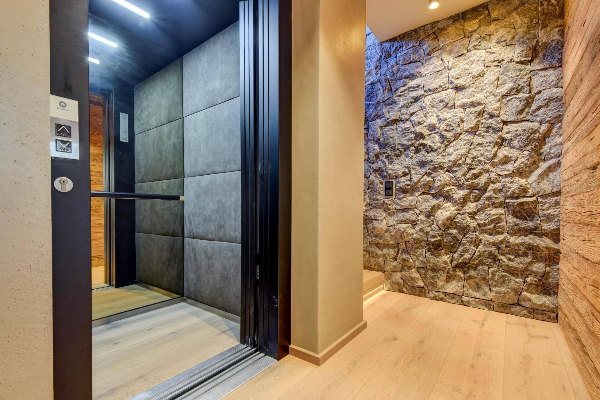 Moderner Eingangsbereich mit Aufzug, Steinwand und Holzboden, elegant und funktional gestaltet.