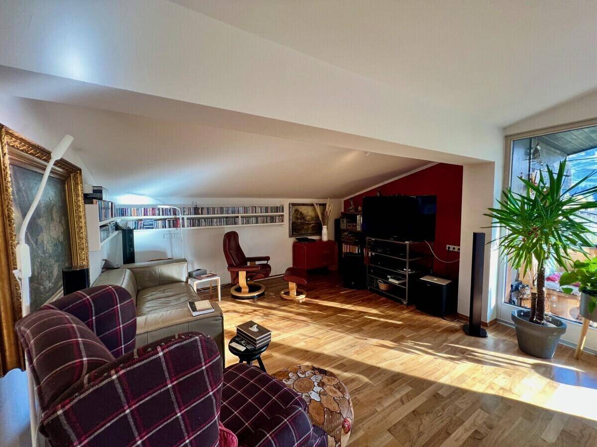 Gemütliches Wohnzimmer mit bequemen Sofas, Fernseher und integrierten Bücherregalen unter der Dachschräge.