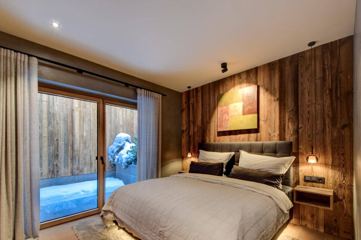 Gemütliches Schlafzimmer mit Holzwand, großem Bett und Zugang zu einem kleinen Außenbereich.