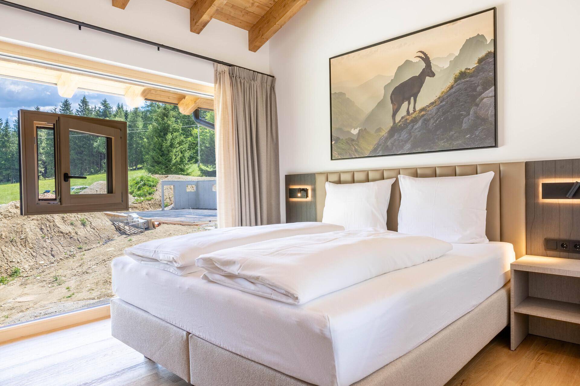 Schlafzimmer mit Doppelbett, Holzboden und großem Fenster mit Blick auf die Baustelle.