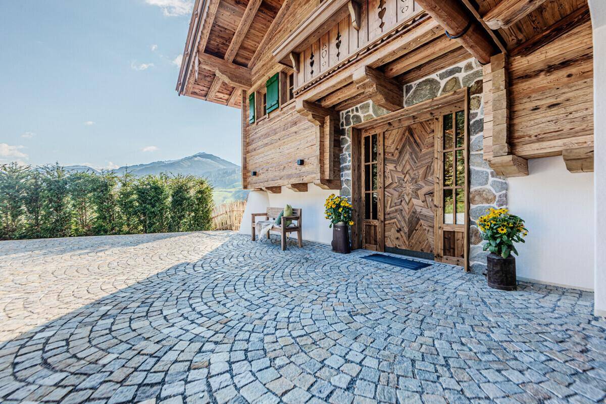 Traditionelles Chalet mit kunstvoll geschnitzter Holztür und gepflastertem Vorplatz in alpiner Umgebung.