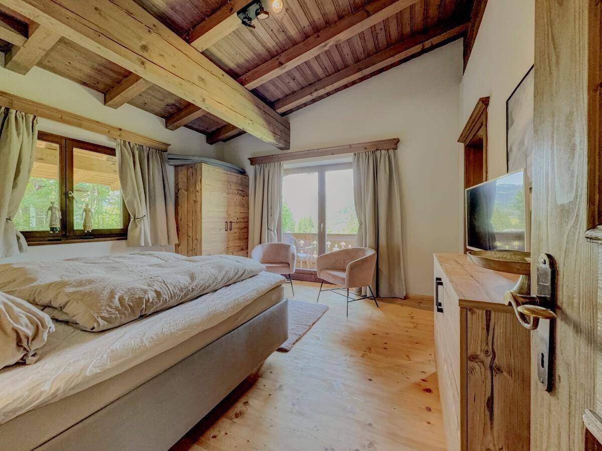 Schlafzimmer mit Holzbalkendecke, TV und Balkonzugang mit Bergblick.