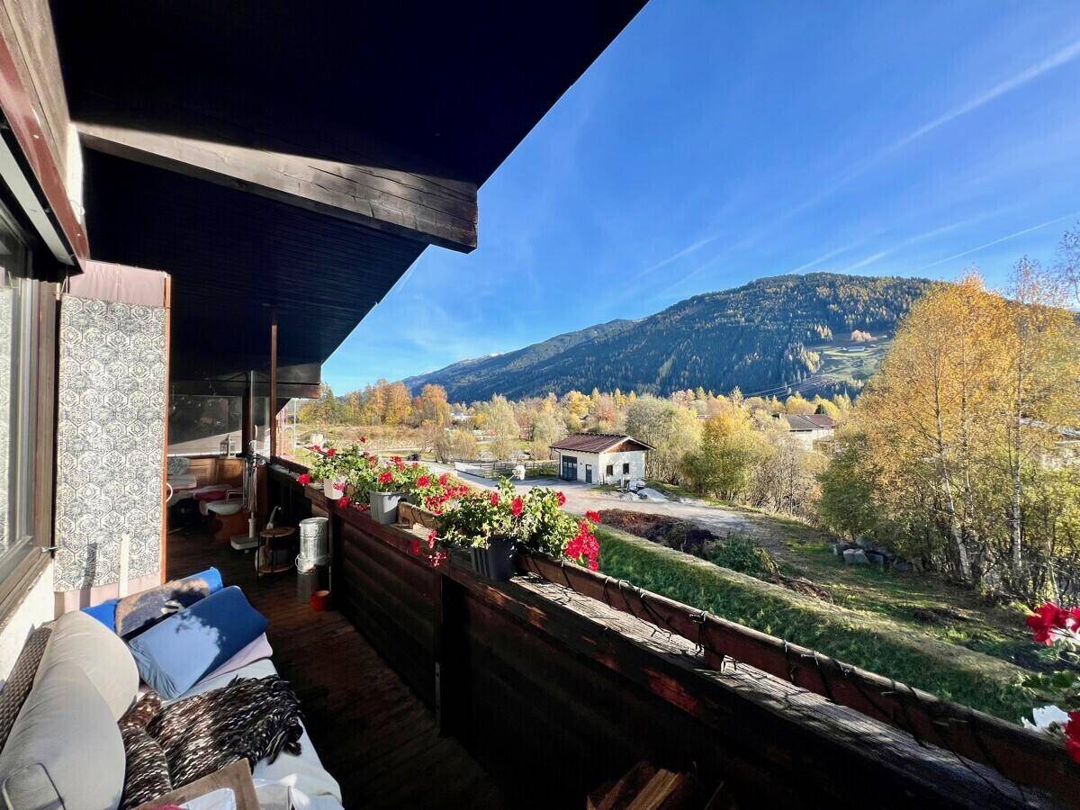 Sonniger Balkon mit bequemer Sitzgelegenheit, Blumenkästen und weitem Bergblick.