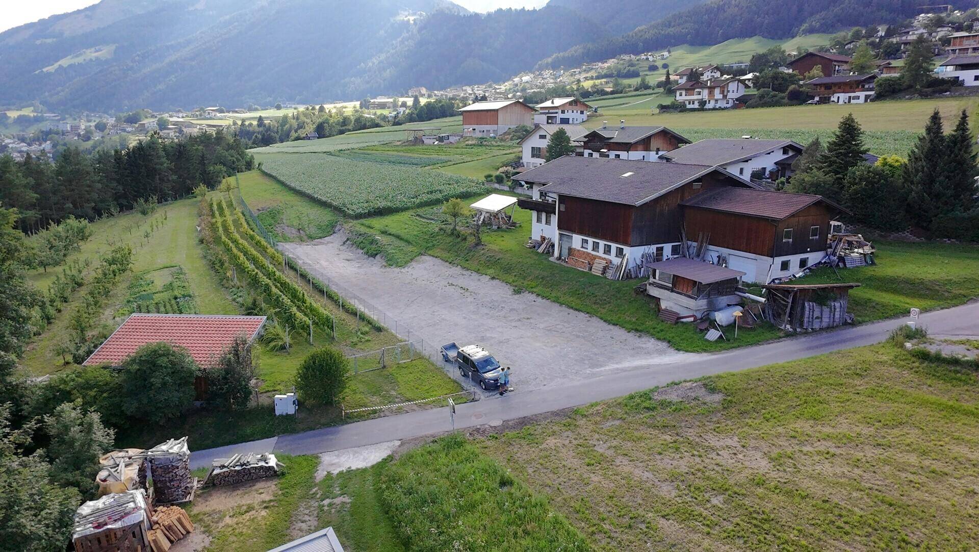 Luftaufnahme einer ländlichen Siedlung mit Feldern, Weinbergen und einem Kiesweg.