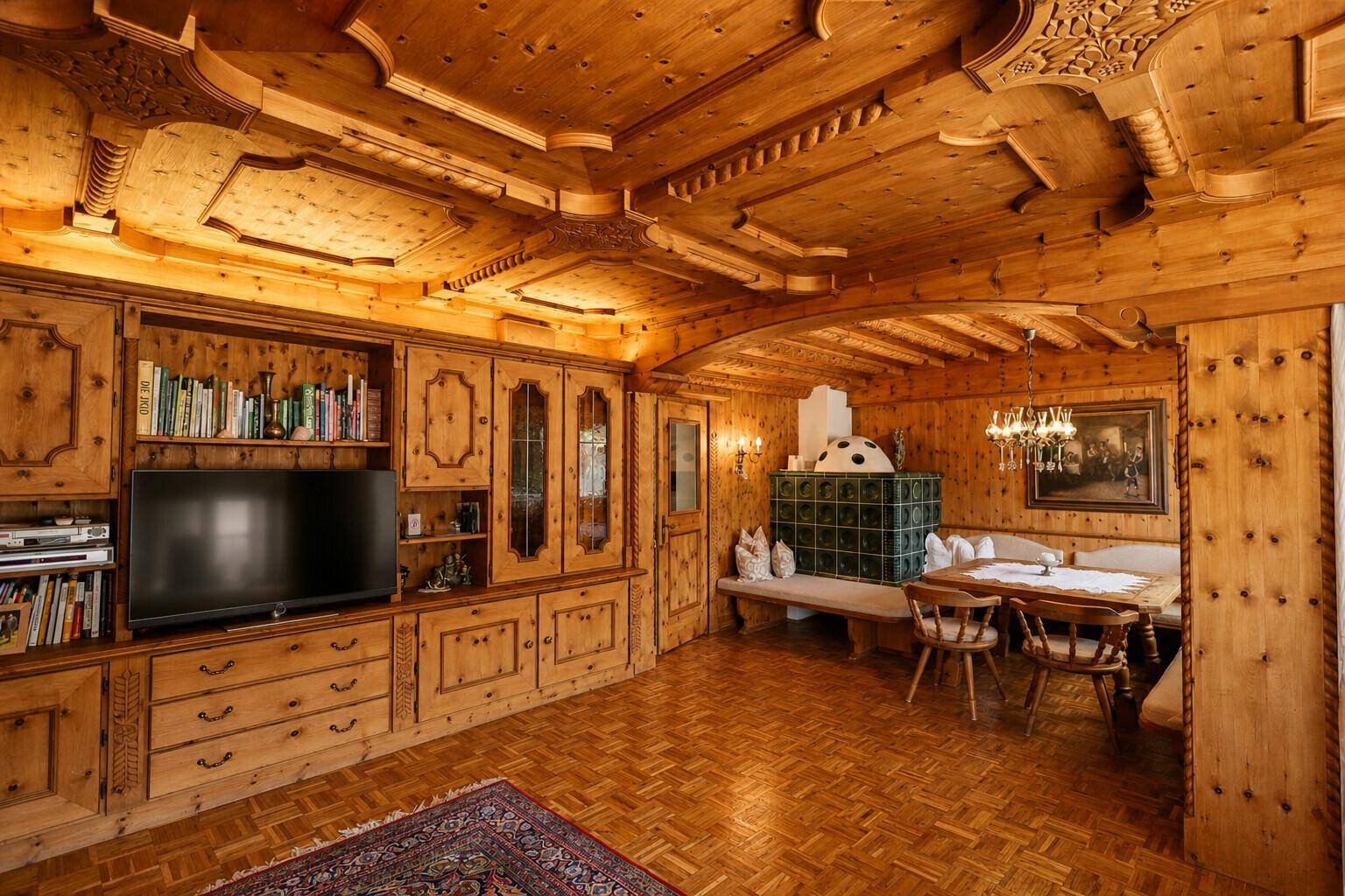 Traditioneller Wohn- und Essbereich im alpinen Stil mit viel Holz, Kachelofen und geschnitzten Details.