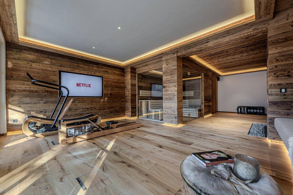 Geräumiger Fitnessbereich mit Holzwänden, modernen Trainingsgeräten und integrierter Sauna.