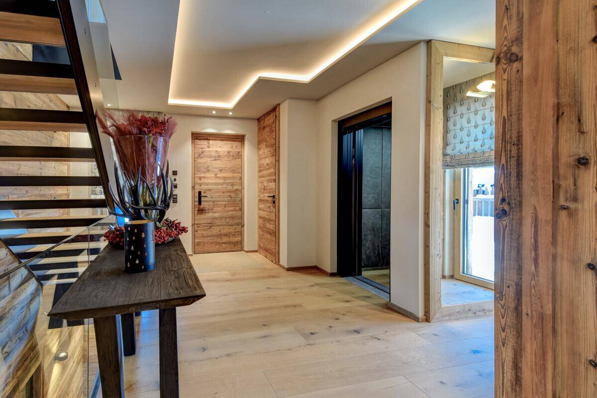 Heller Flur mit Holzboden, Aufzug und moderner Treppe mit Glasgeländer.