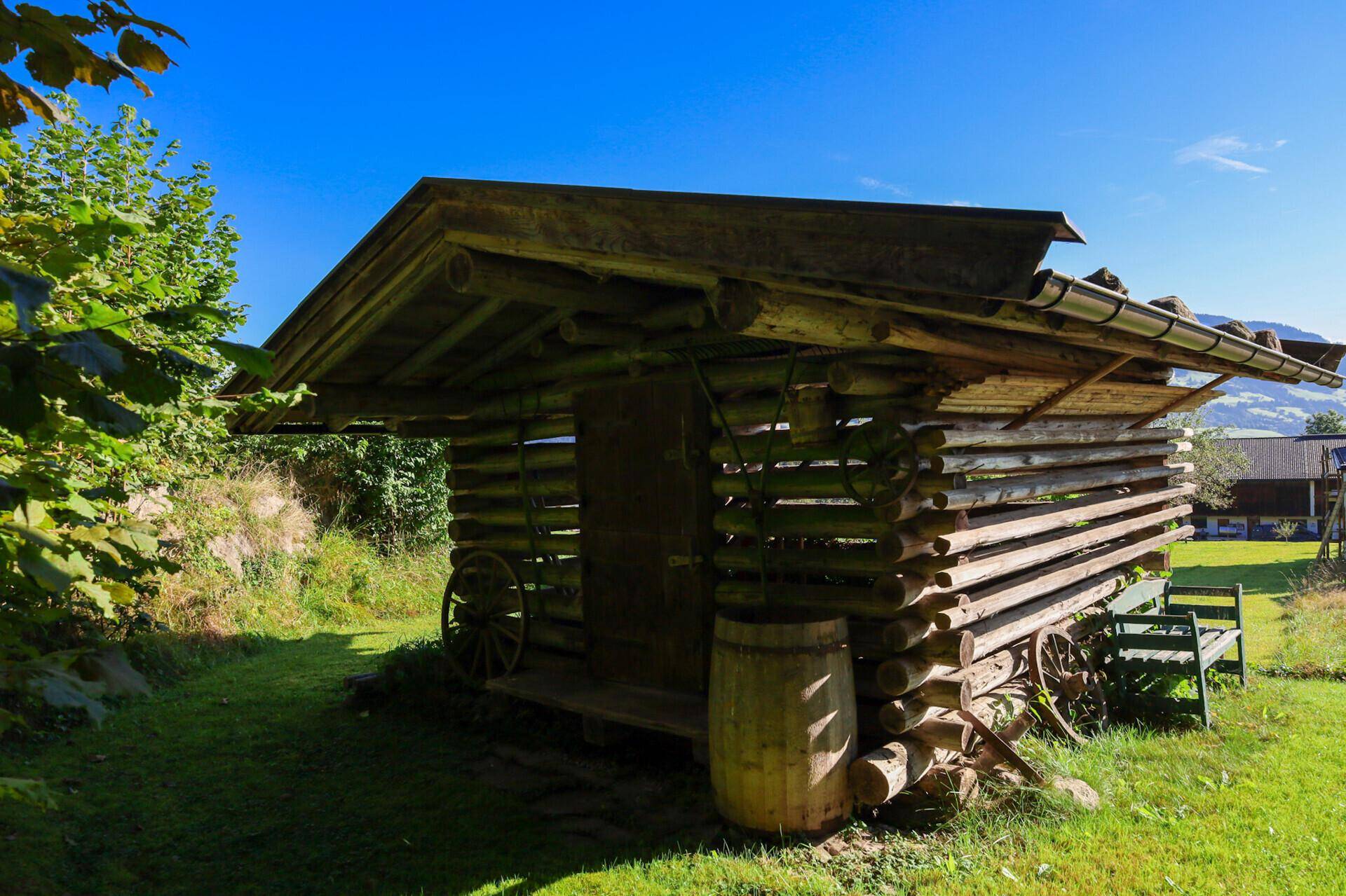 Rustikale Holzhütte im Garten, umgeben von Grünflächen unter strahlend blauem Himmel.