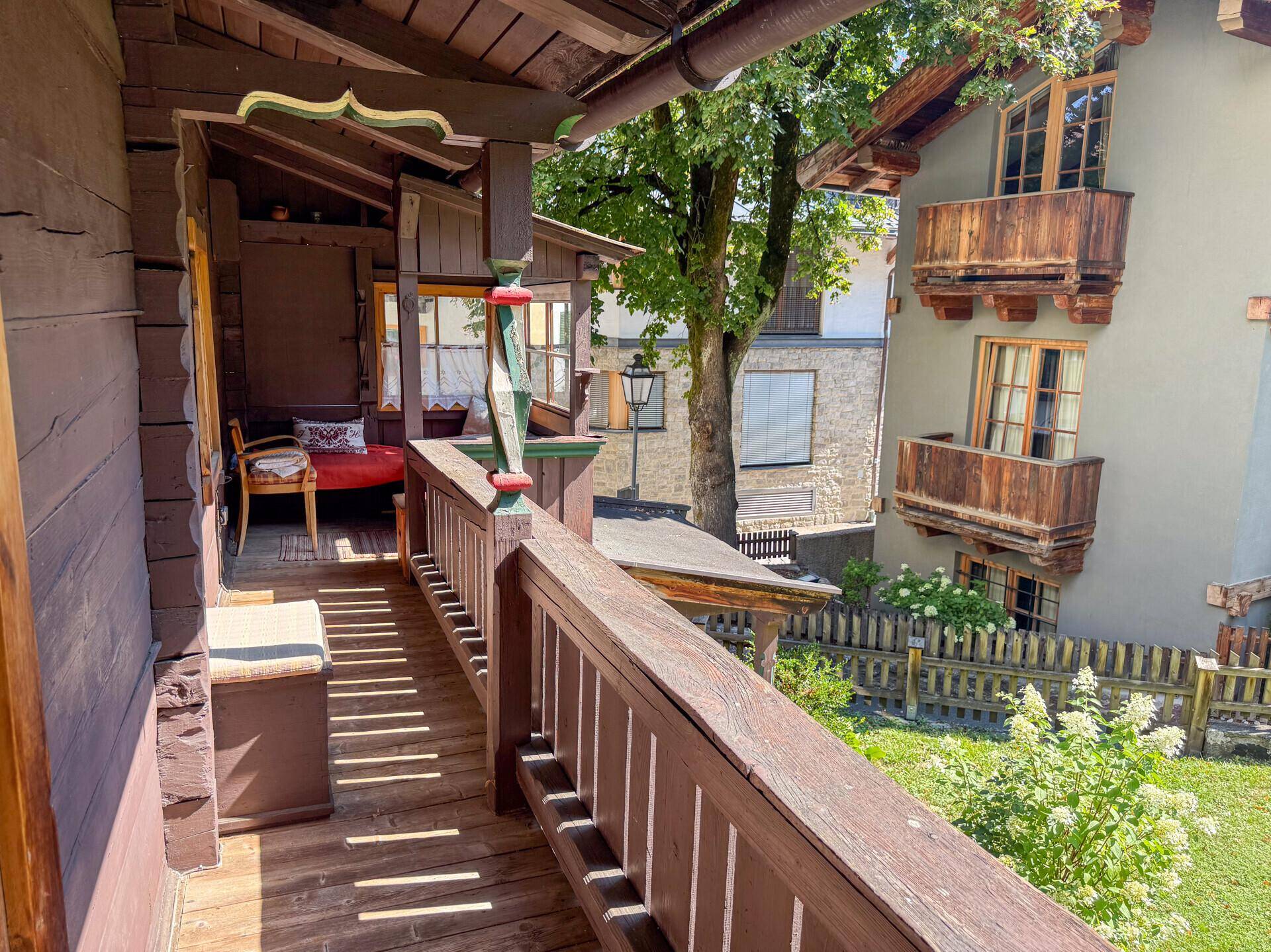 Traditioneller Holzbalkon mit rustikalem Geländer und Blick auf die umliegenden Gebäude und den Garten.