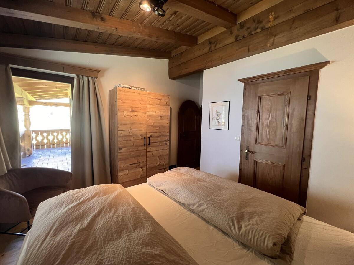 Schlafzimmer mit rustikalem Holzschrank, Holzbalkendecke und Zugang zu einem Balkon.