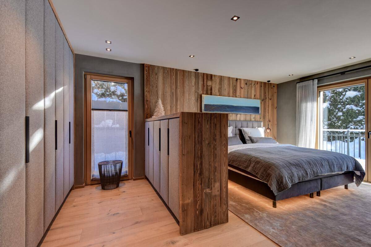 Geräumiges Schlafzimmer mit Holzwand, Einbauschränken und großem Bett mit indirekter Beleuchtung.