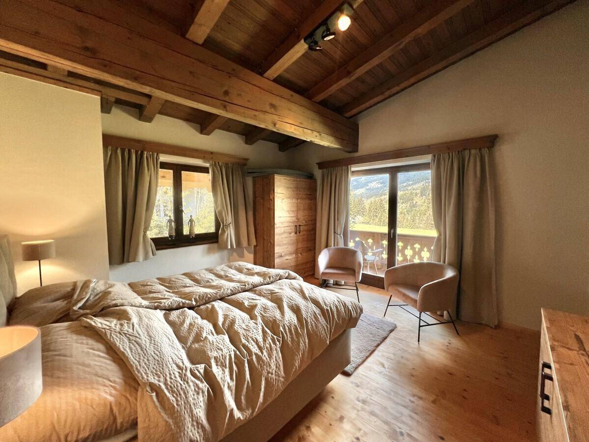 Gemütliches Schlafzimmer mit Holzbalkendecke, Doppelbett und Zugang zu einem Balkon mit Bergblick.