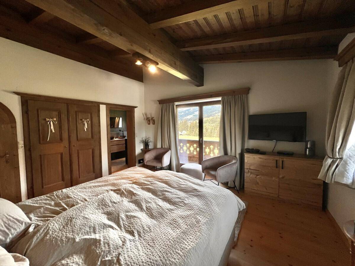 Schlafzimmer mit Holzbalkendecke, großem Holzschrank und Balkonzugang mit Bergblick.