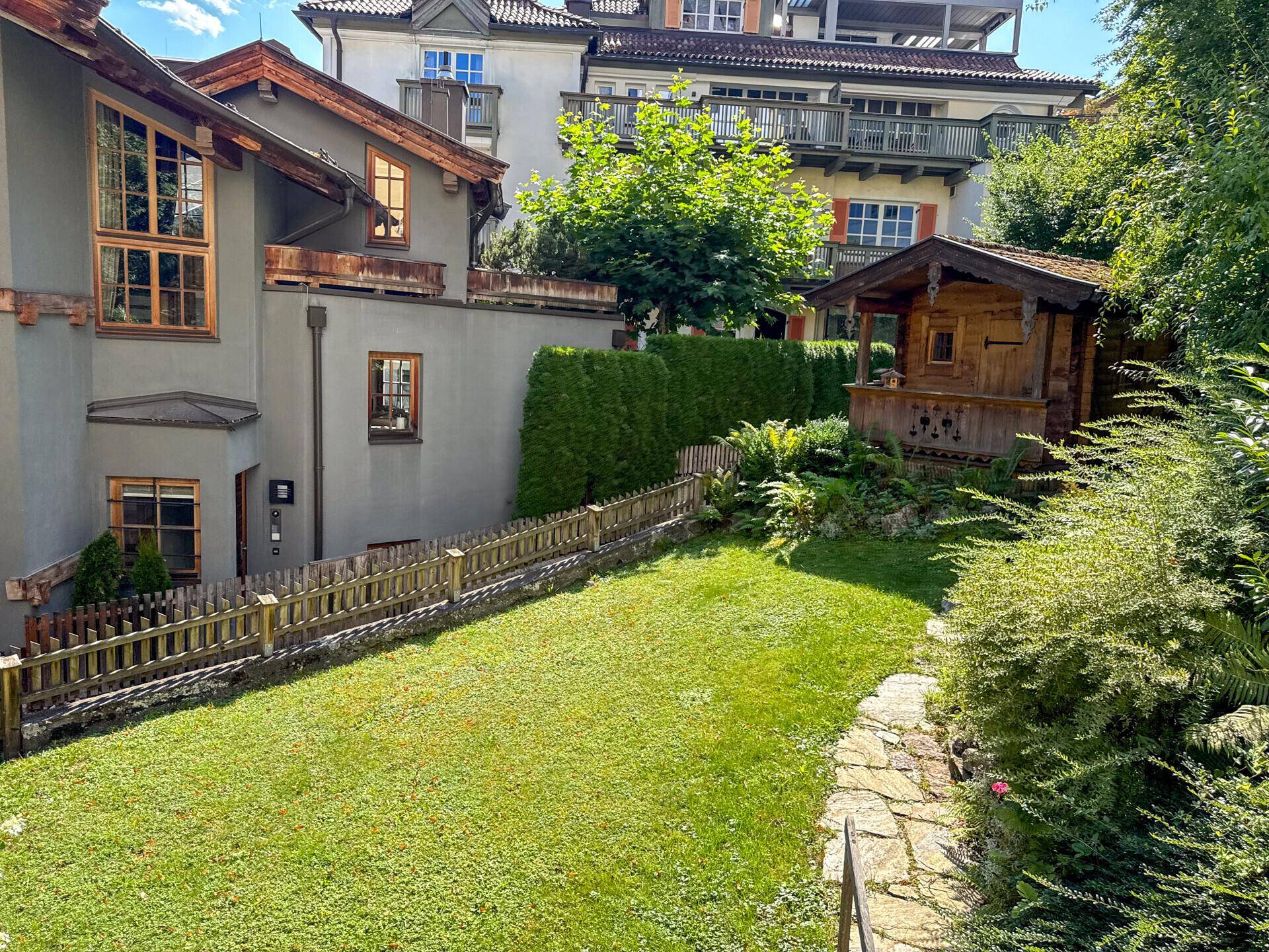 Gepflegter Gartenbereich mit Rasenfläche, einem kleinen Holzschuppen und umgebenden Gebäuden.