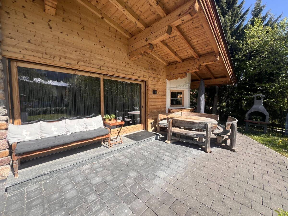 Gepflasterte Terrasse mit rustikalen Holzmöbeln und einem Grillbereich neben dem Holzhaus.