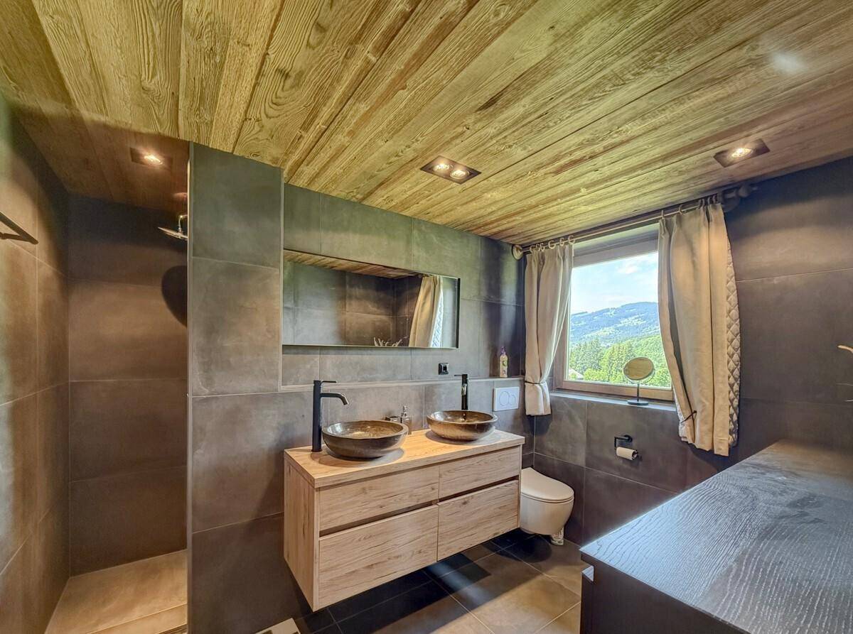 Modernes Badezimmer mit Holzbalkendecke, doppelten Waschbecken und großer Dusche, mit Bergblick durch das Fenster.