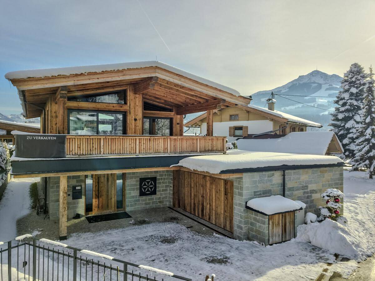 Neubau-Chalet mit Holzverkleidung und Steinelementen, umgeben von Schnee und Bergen.