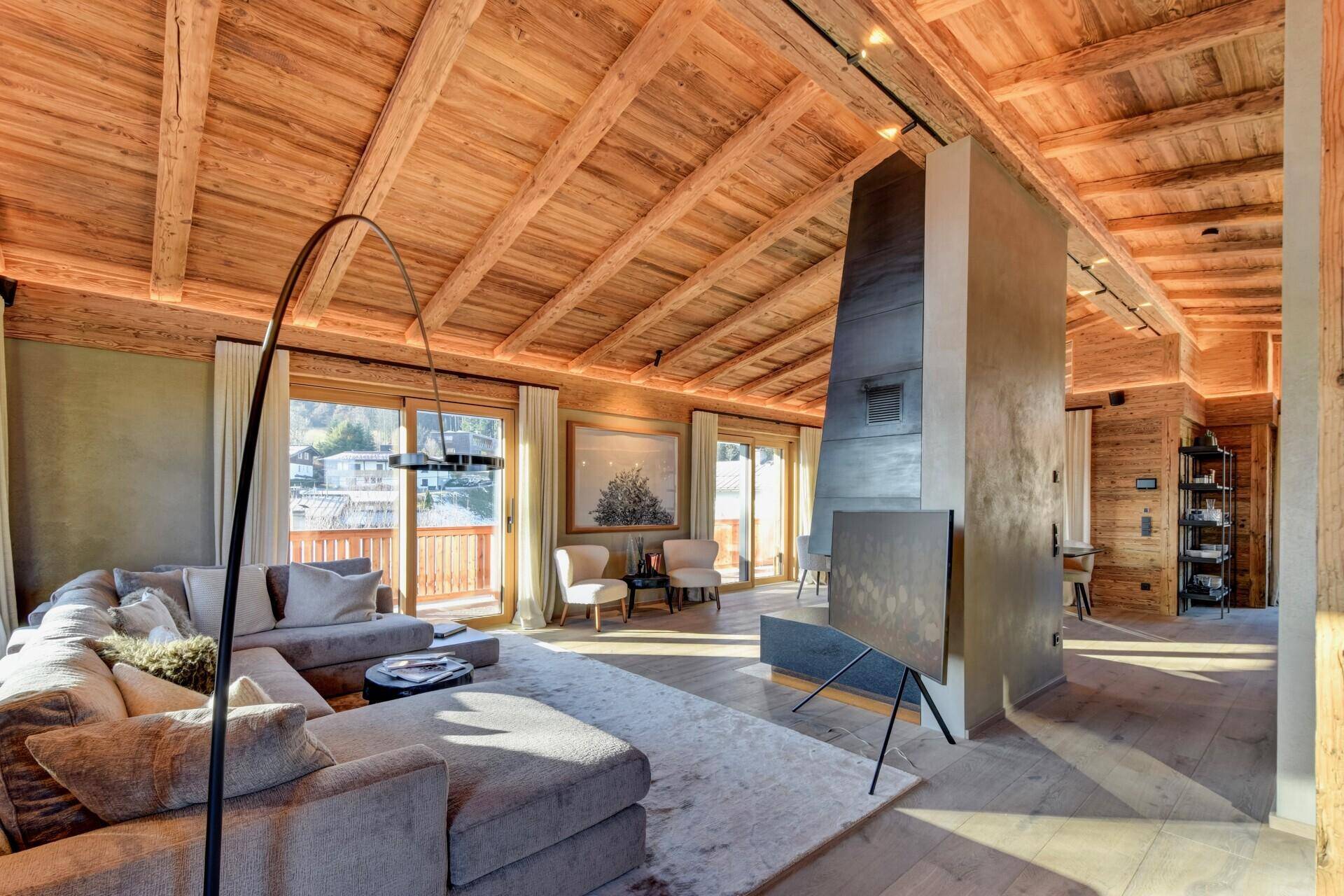Gemütliches Wohnzimmer im alpinen Stil mit Holzbalkendecke, Kamin und Zugang zum Balkon.