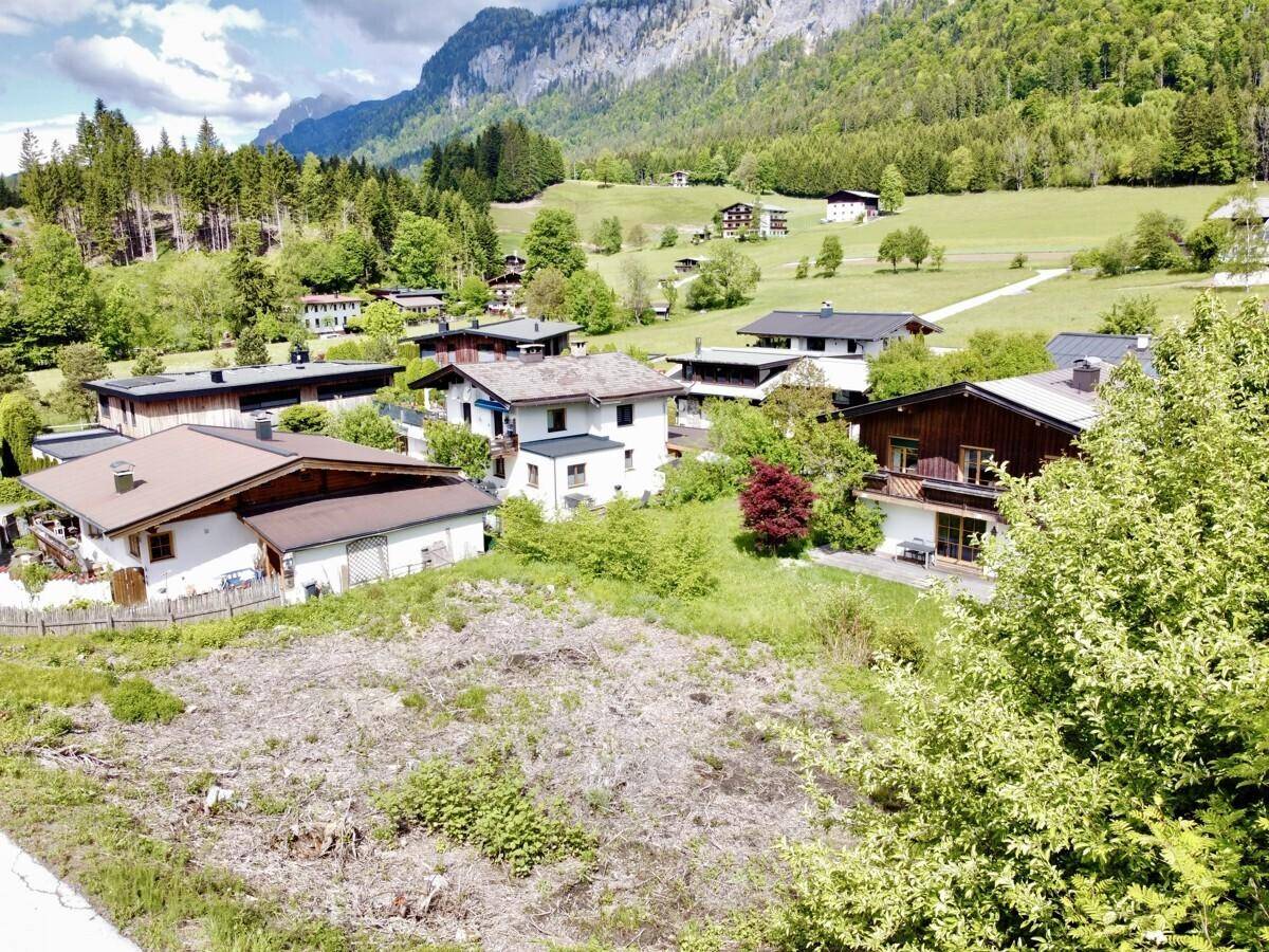Blick über eine ländliche Siedlung mit Häusern und grüner Umgebung, umgeben von Bergen.