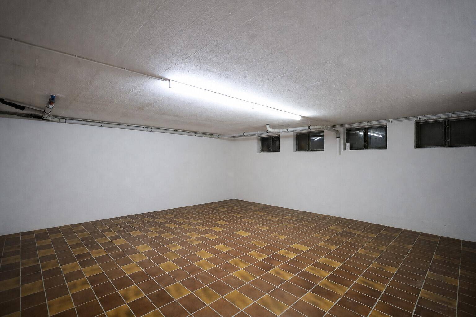 Geräumiger Kellerraum mit Fliesenboden und kleinen Fenstern, ideal als Lagerfläche.
