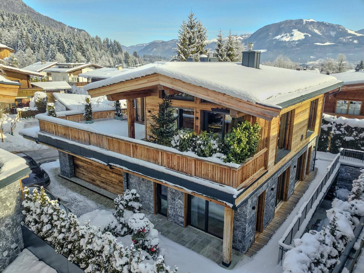 Modernes Chalet mit Holzfassade und Steinelementen, umgeben von verschneiter Berglandschaft.