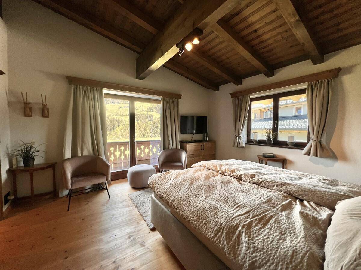Geräumiges Schlafzimmer mit Holzbalkendecke, Sitzgelegenheiten und Balkonzugang mit Bergblick.