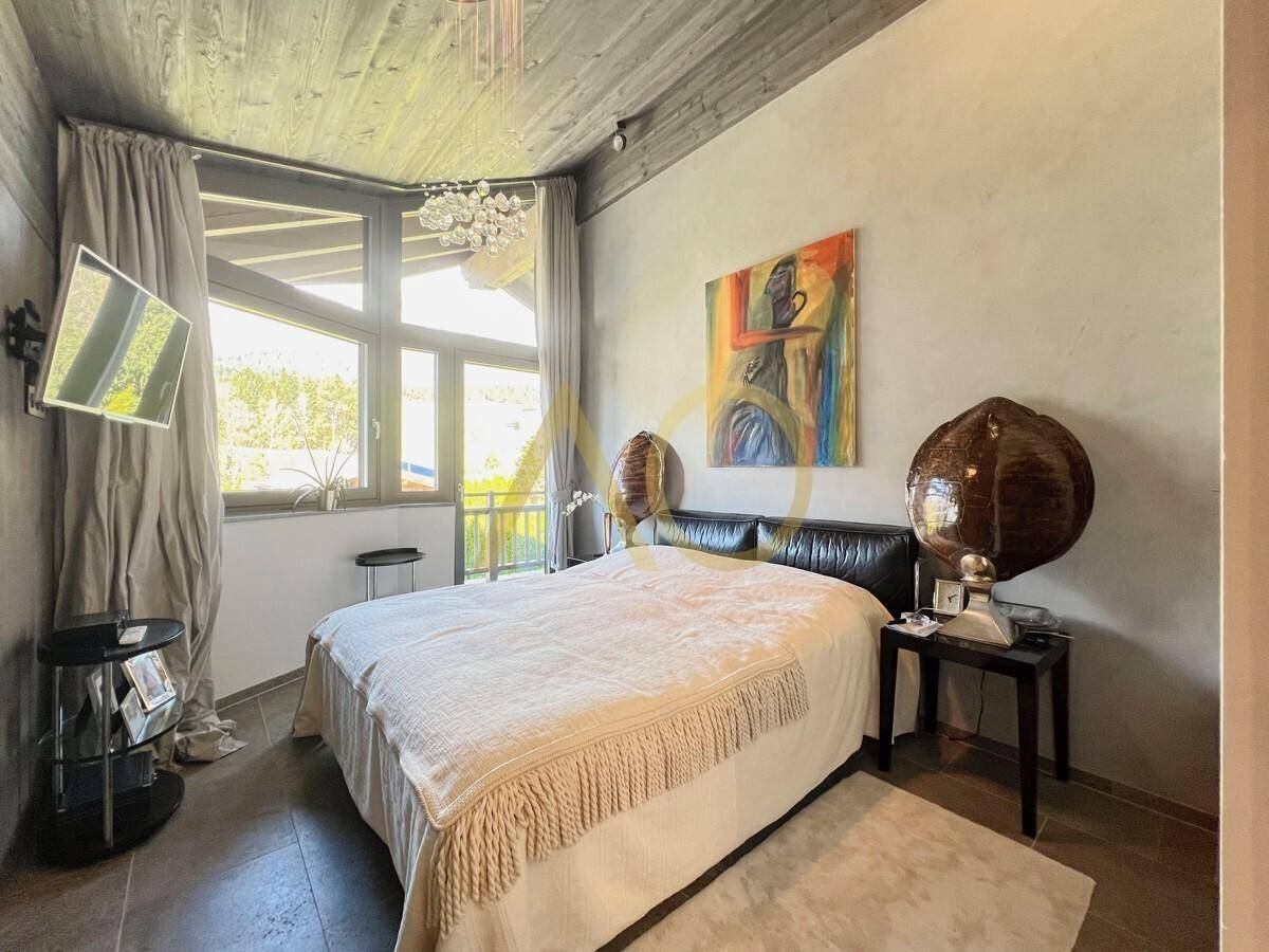 Gemütliches Schlafzimmer mit Holzbalkendecke, großen Fenstern und viel Tageslicht.