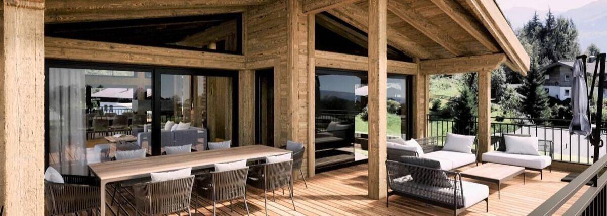 Geräumige Holzterrasse mit Ess- und Loungebereich, umgeben von grüner Berglandschaft.