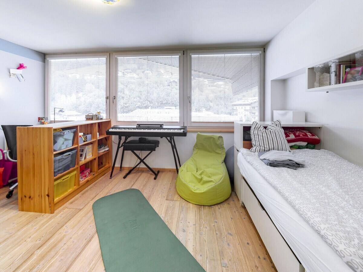 Helles Kinderzimmer mit Bett, Schreibtisch, Keyboard und großen Fenstern.