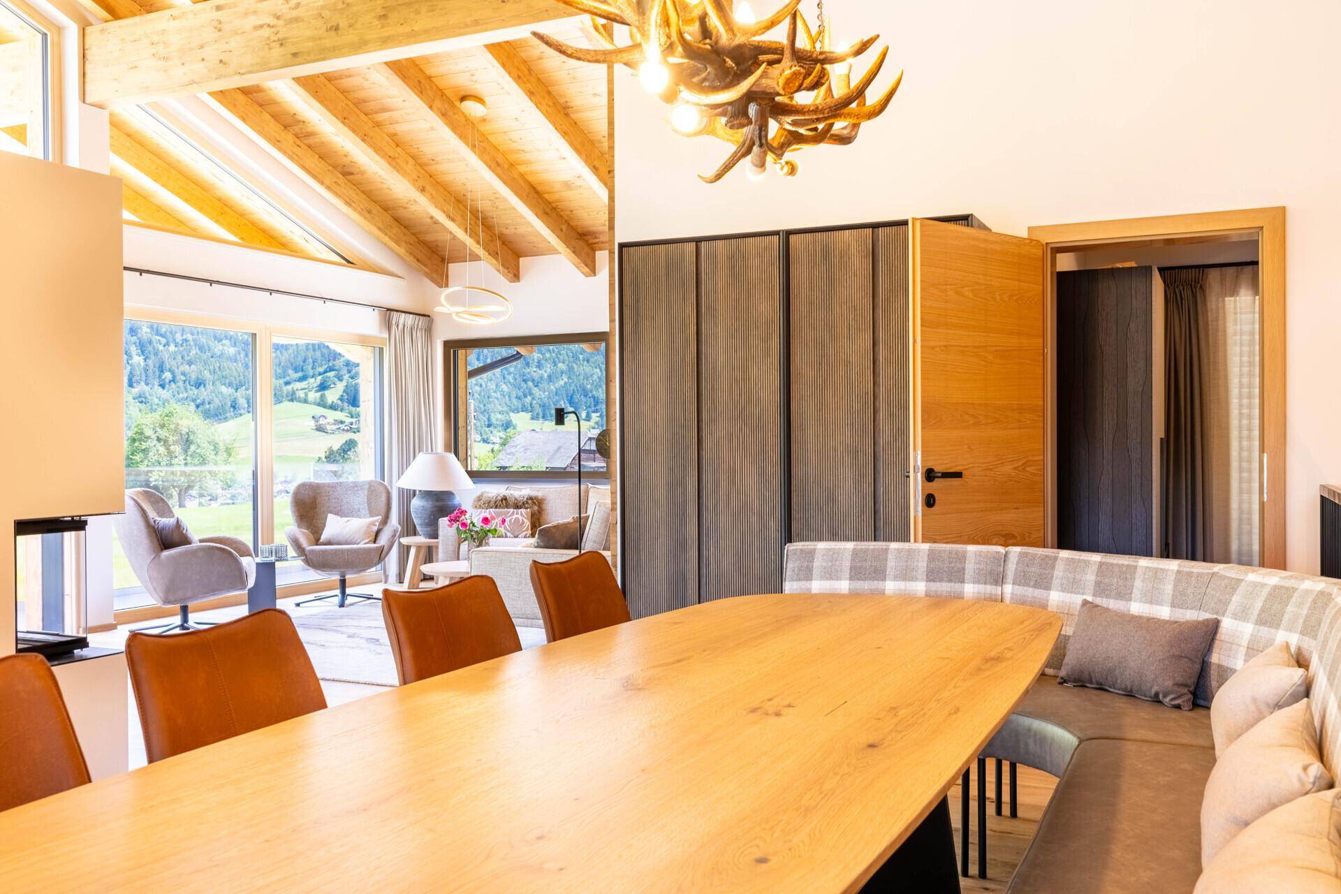 Essbereich mit Holztisch, Sitzbank und Blick auf den Wohnbereich und die Natur.