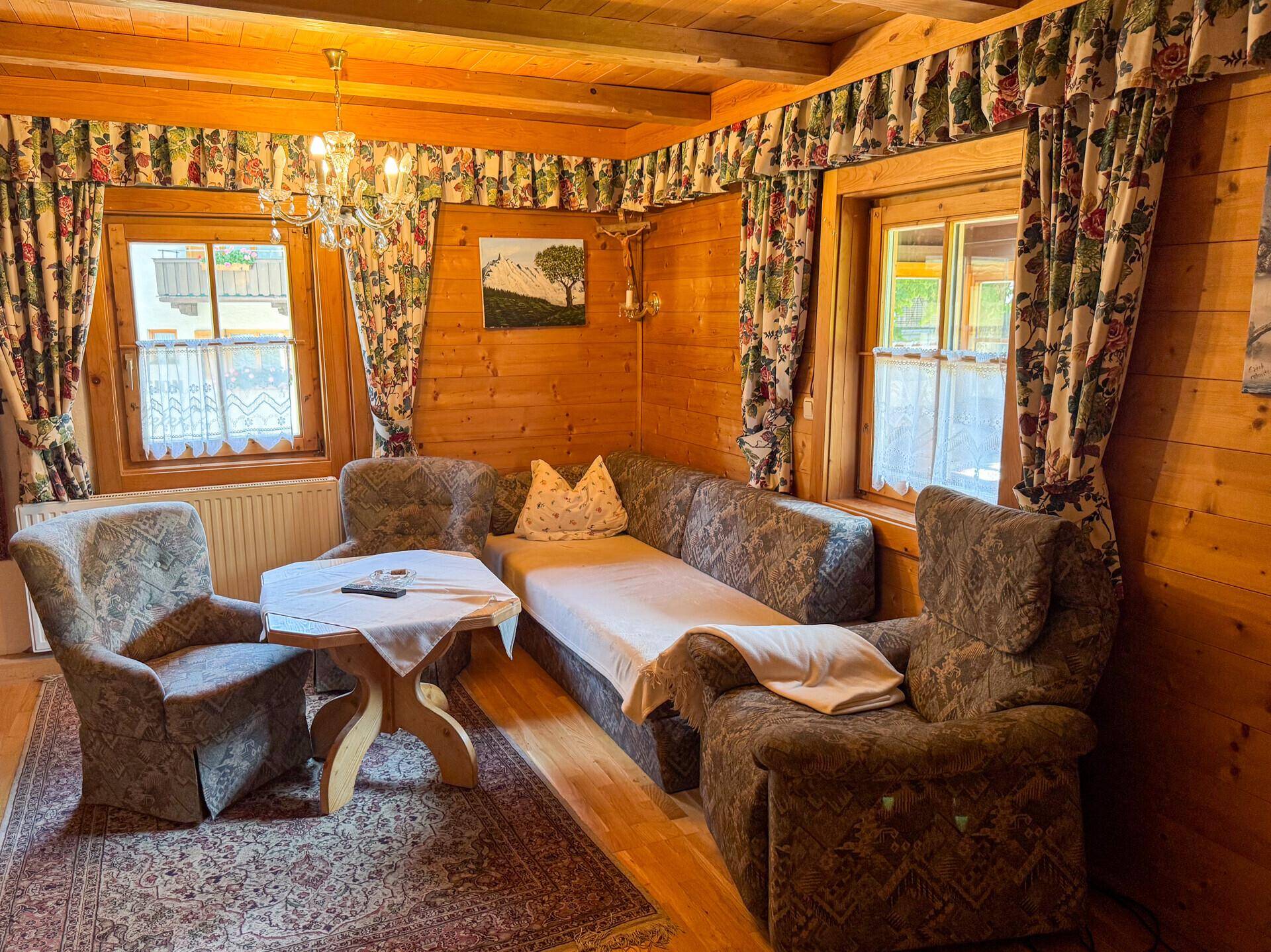 Traditionelles Wohnzimmer mit holzvertäfelten Wänden, gemusterten Möbeln und floralen Vorhängen.