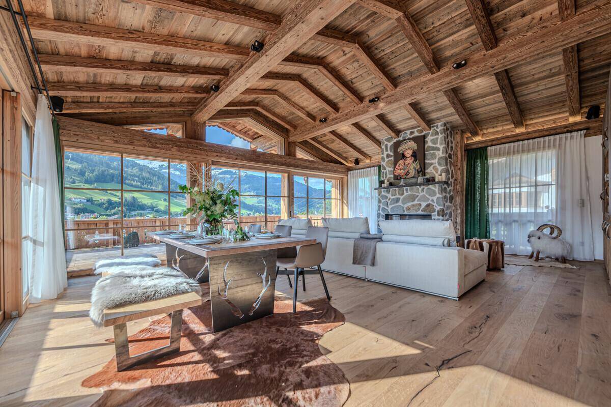 Großzügiger Wohn-Essbereich mit Kamin, Holzbalkendecke und weitem Blick auf die alpine Landschaft.