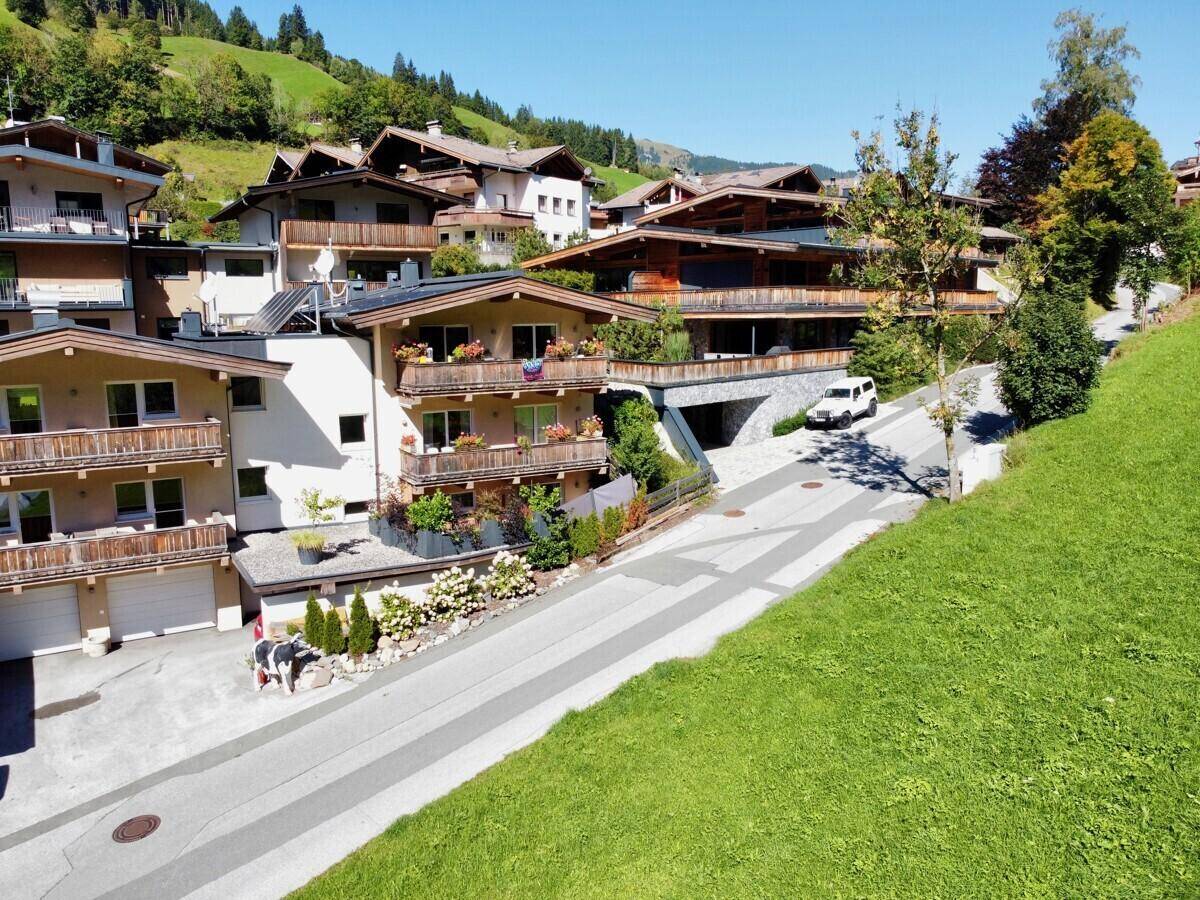 Wohngebiet mit mehreren Häusern im alpinen Stil, umgeben von grünen Hügeln.