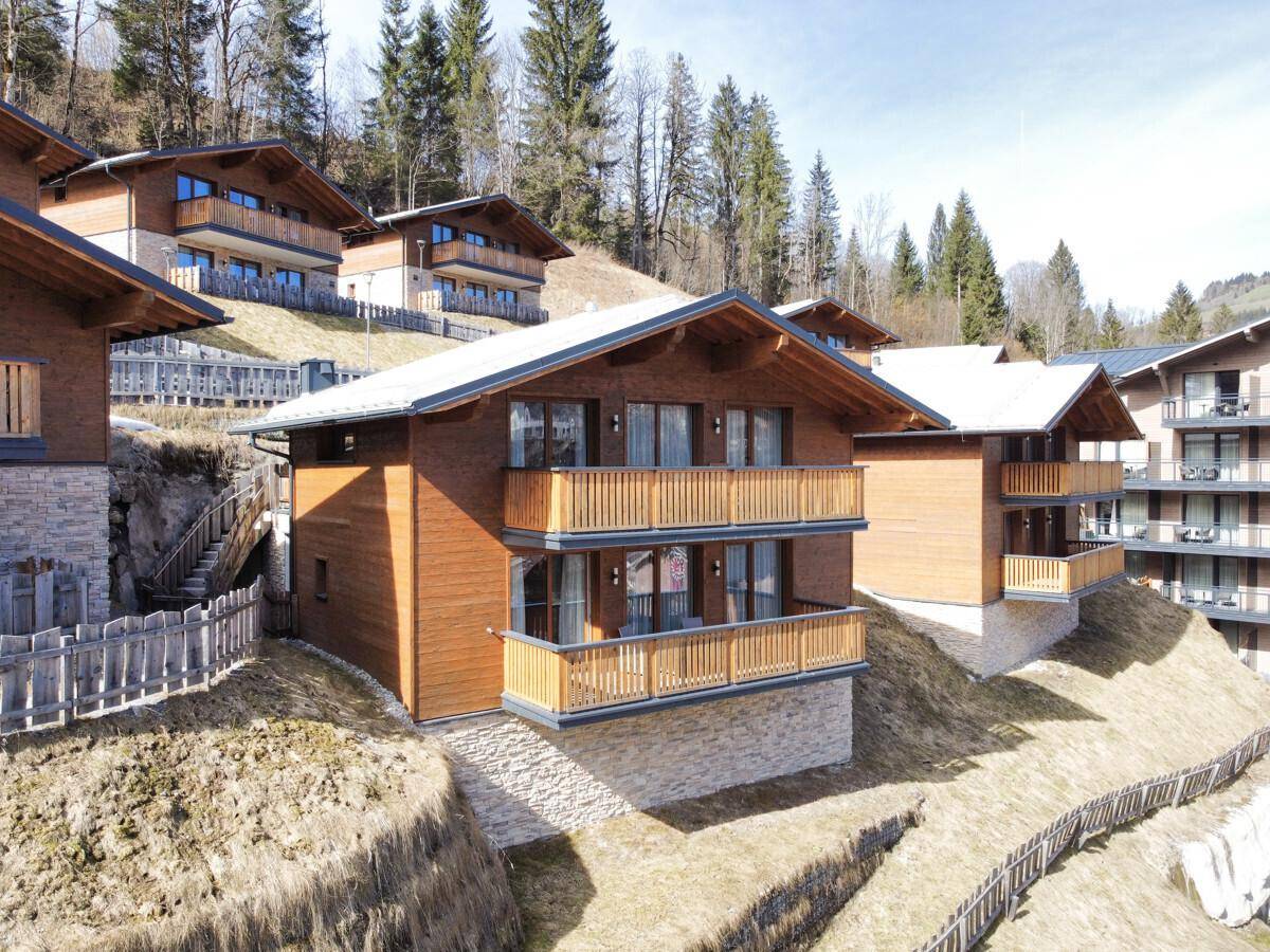Moderne Chalets mit Holzfassaden und Steinverkleidung, terrassenförmig am Hang gelegen mit Bergblick.