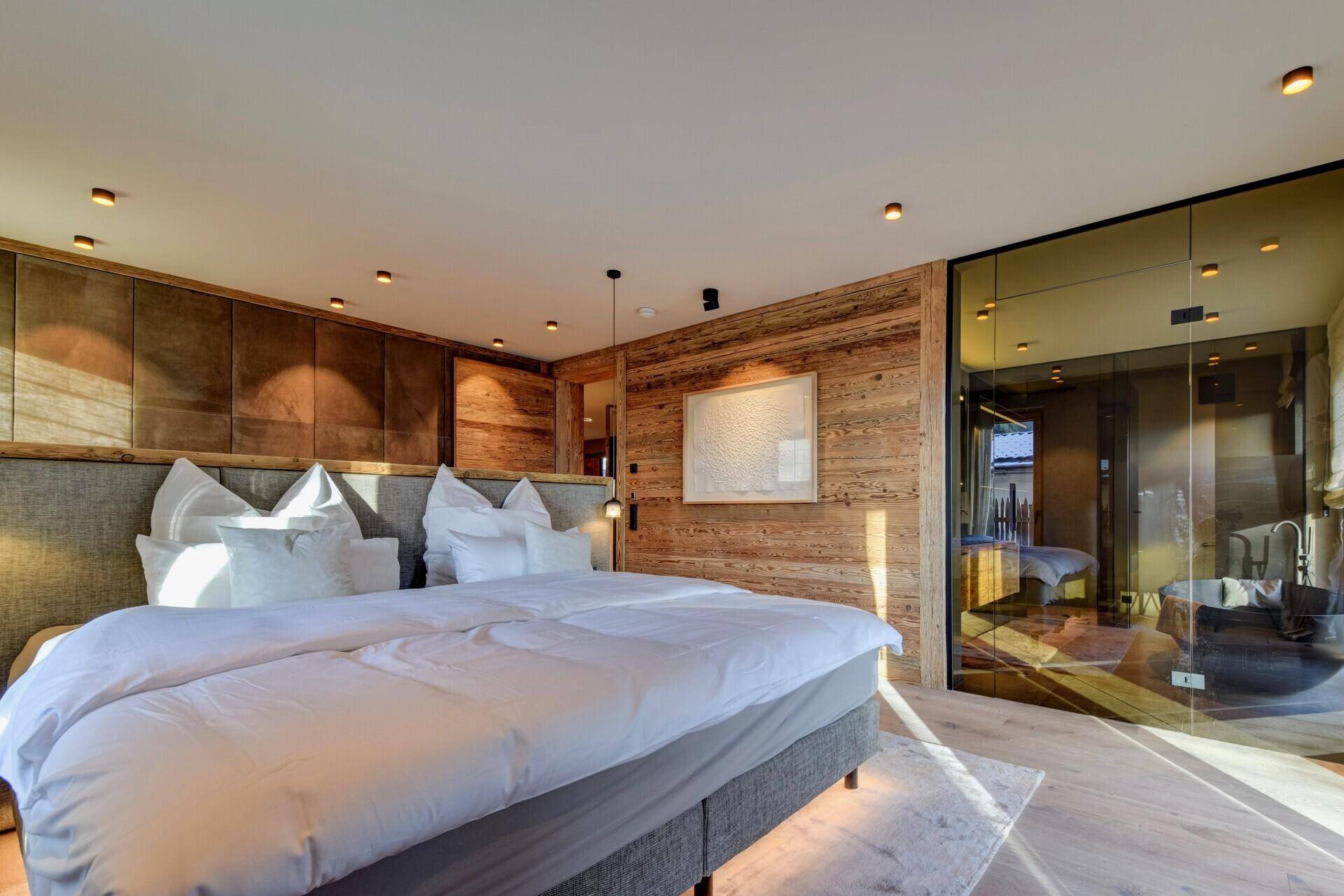 Modernes Schlafzimmer mit Holzwänden, integriertem Badbereich und viel natürlichem Licht.