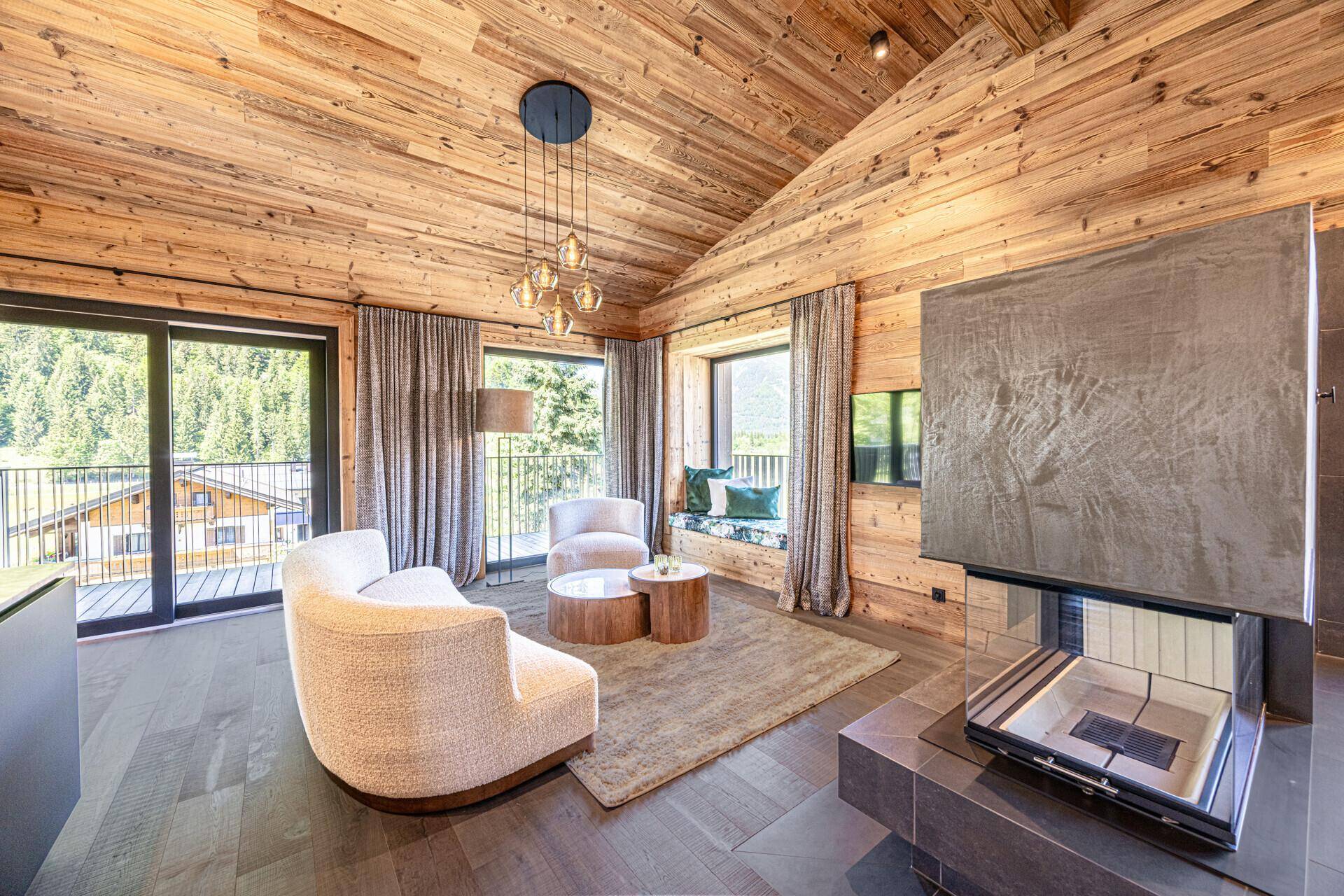 Geräumiges Wohnzimmer mit Kamin, Holzbalkendecke und Zugang zu einem Balkon mit Bergblick.