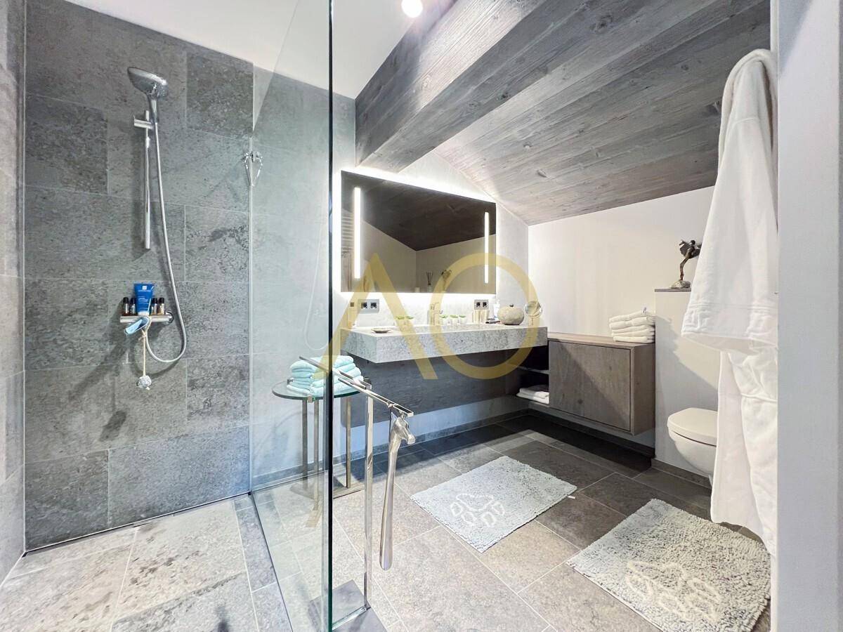 Modernes Badezimmer mit großer begehbarer Dusche, Doppelwaschtisch und beleuchtetem Spiegel.