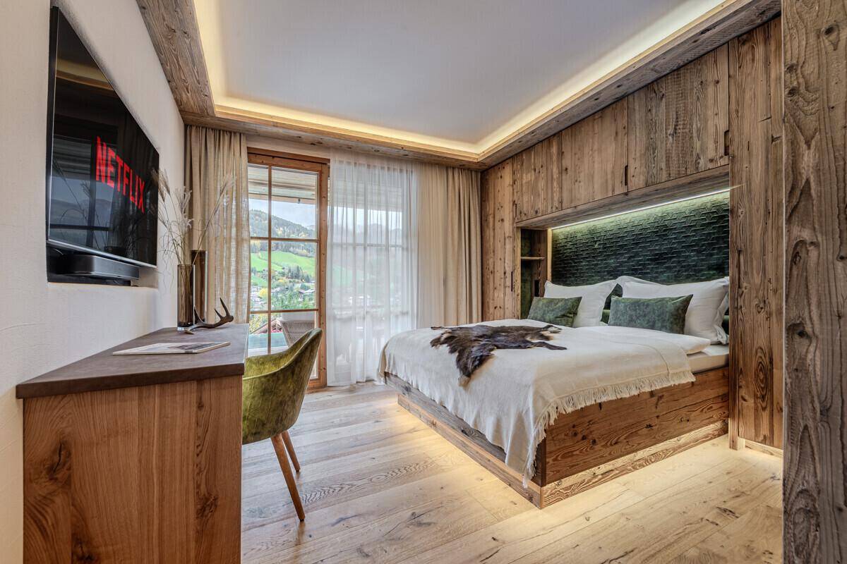Komfortables Schlafzimmer mit Holzeinrichtung, Schreibtisch und Blick auf die grüne Landschaft.