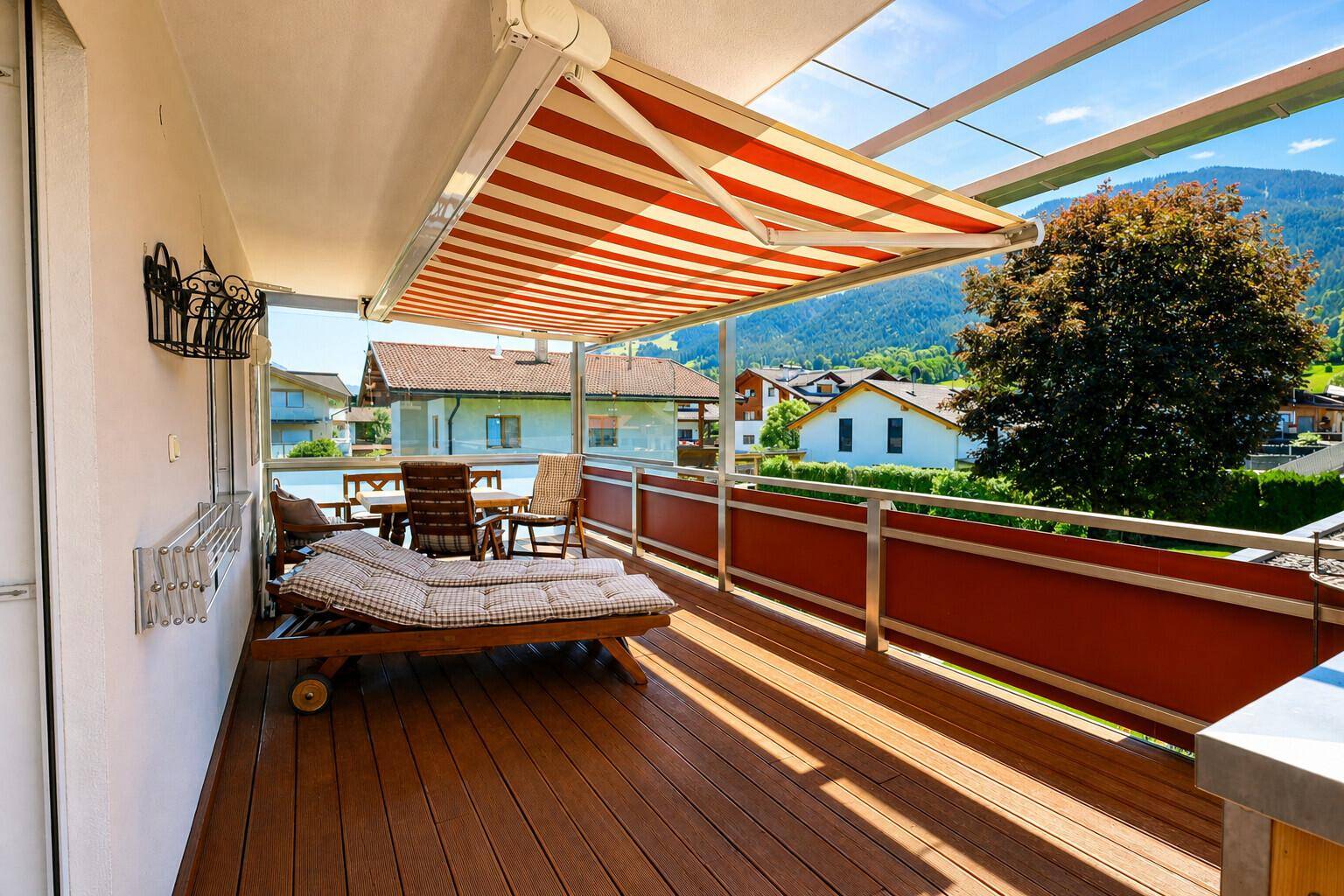Großer Balkon mit Holzdeck, ausziehbarer Markise und Essbereich im Freien mit Bergblick.