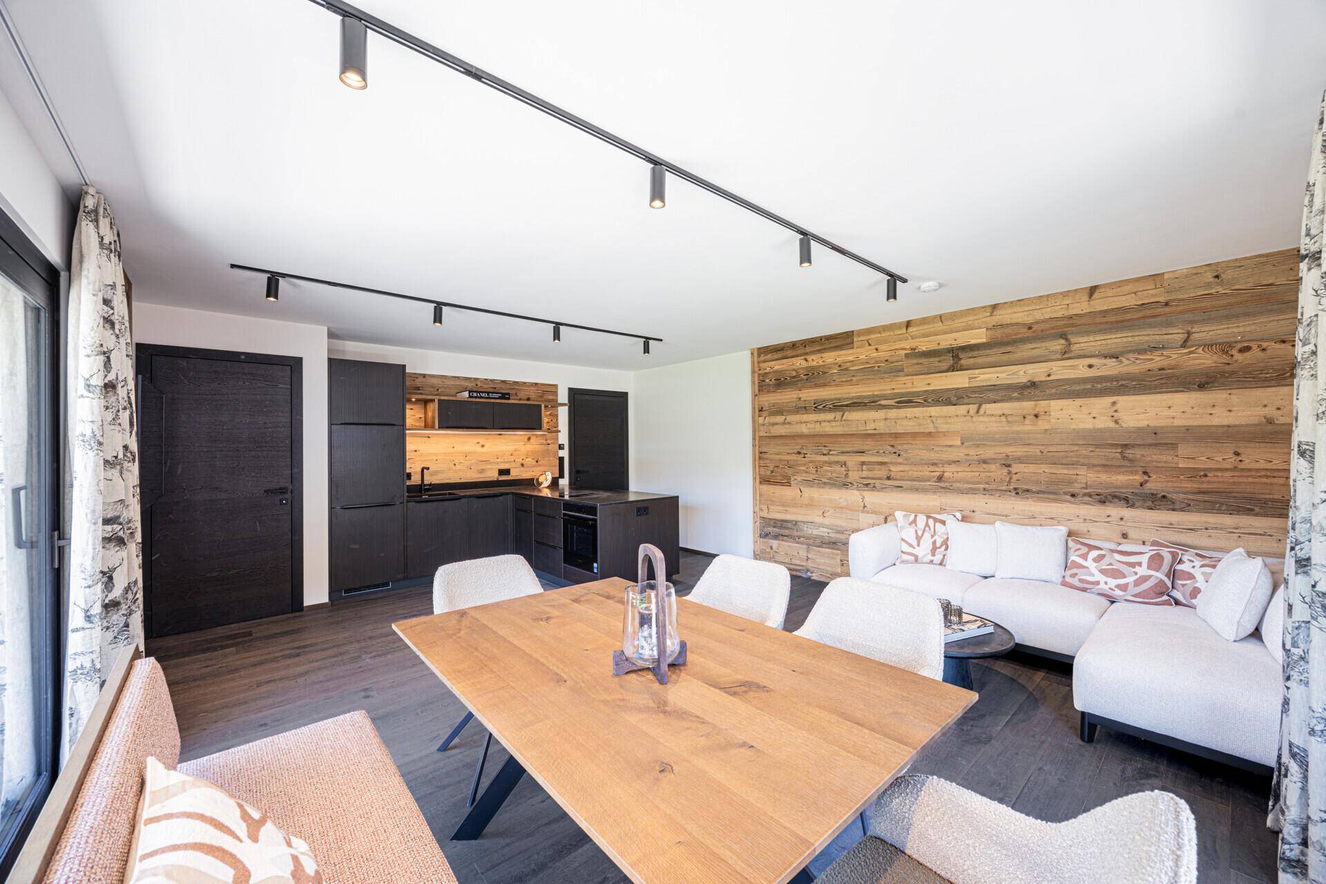 Gemütlicher Wohn- und Essbereich mit Holztisch, bequemer Couch und moderner Küche im Hintergrund.