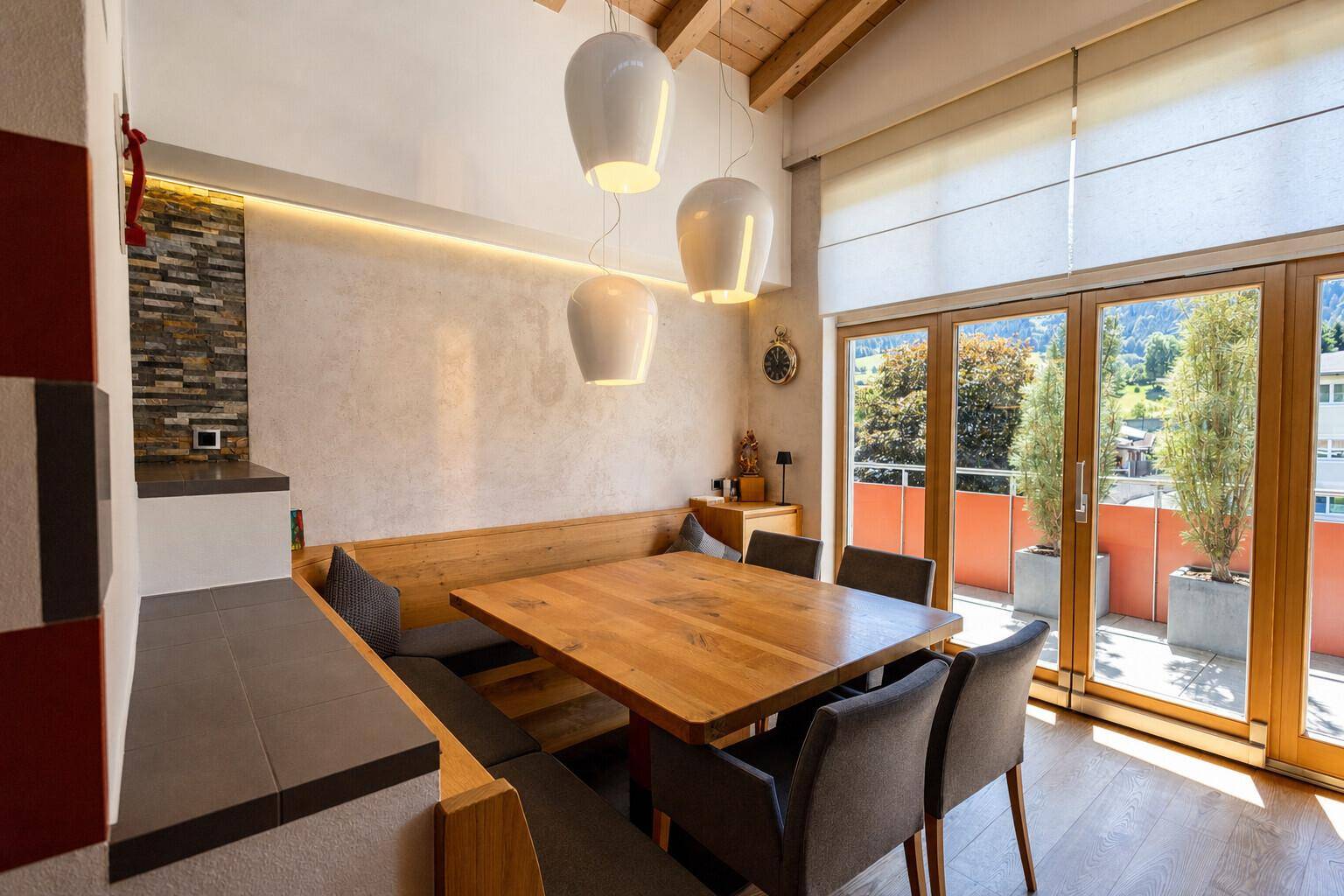 Heller Essbereich mit Holztisch, Eckbank und Zugang zu einem Balkon mit Bergblick.