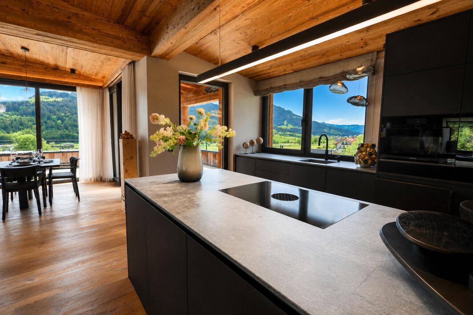 Moderne offene Küche mit dunklen Fronten, Kochinsel und Essbereich mit Bergblick.