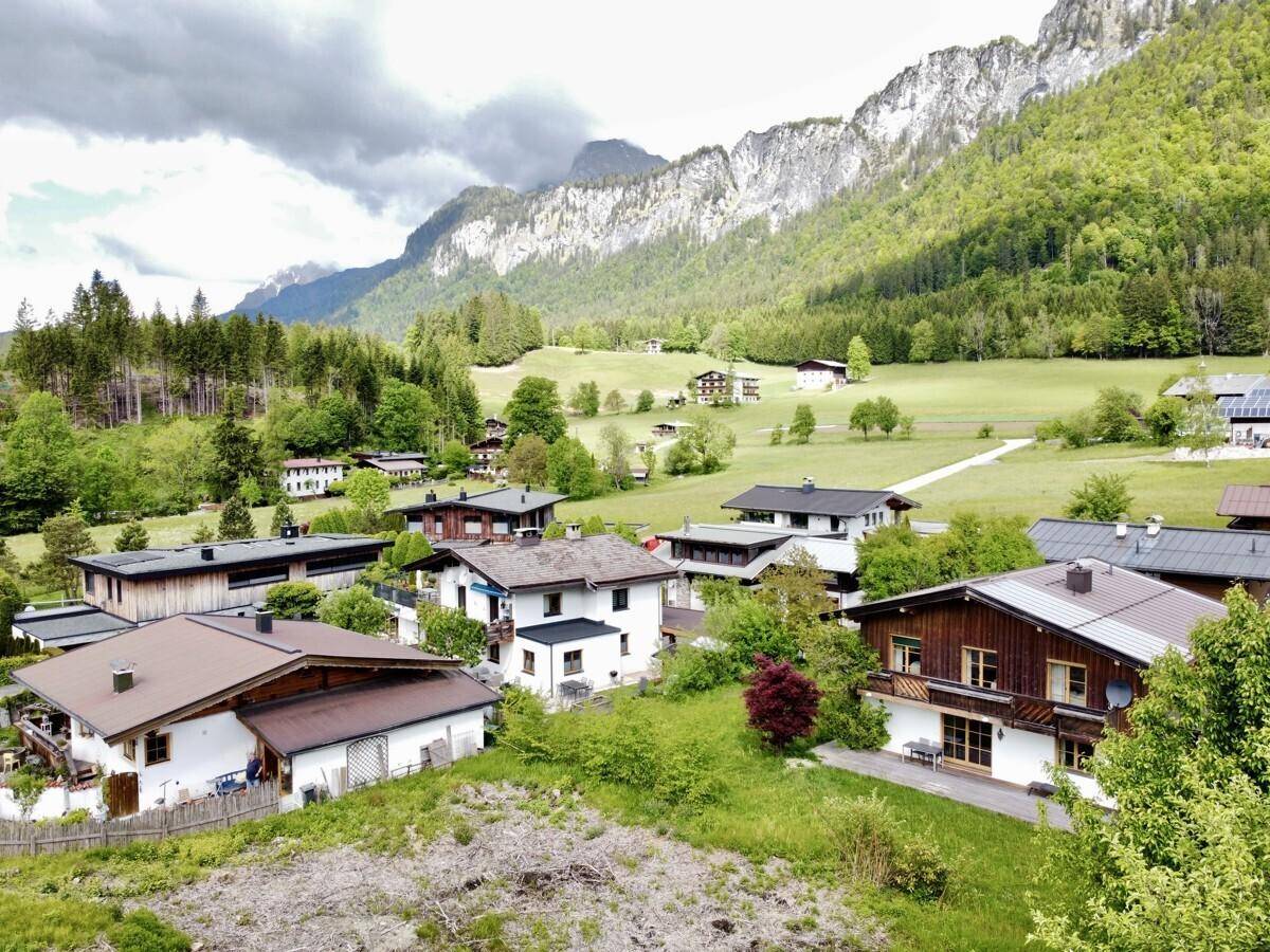 Blick über eine ländliche Siedlung mit Häusern und grüner Umgebung, umgeben von Bergen.