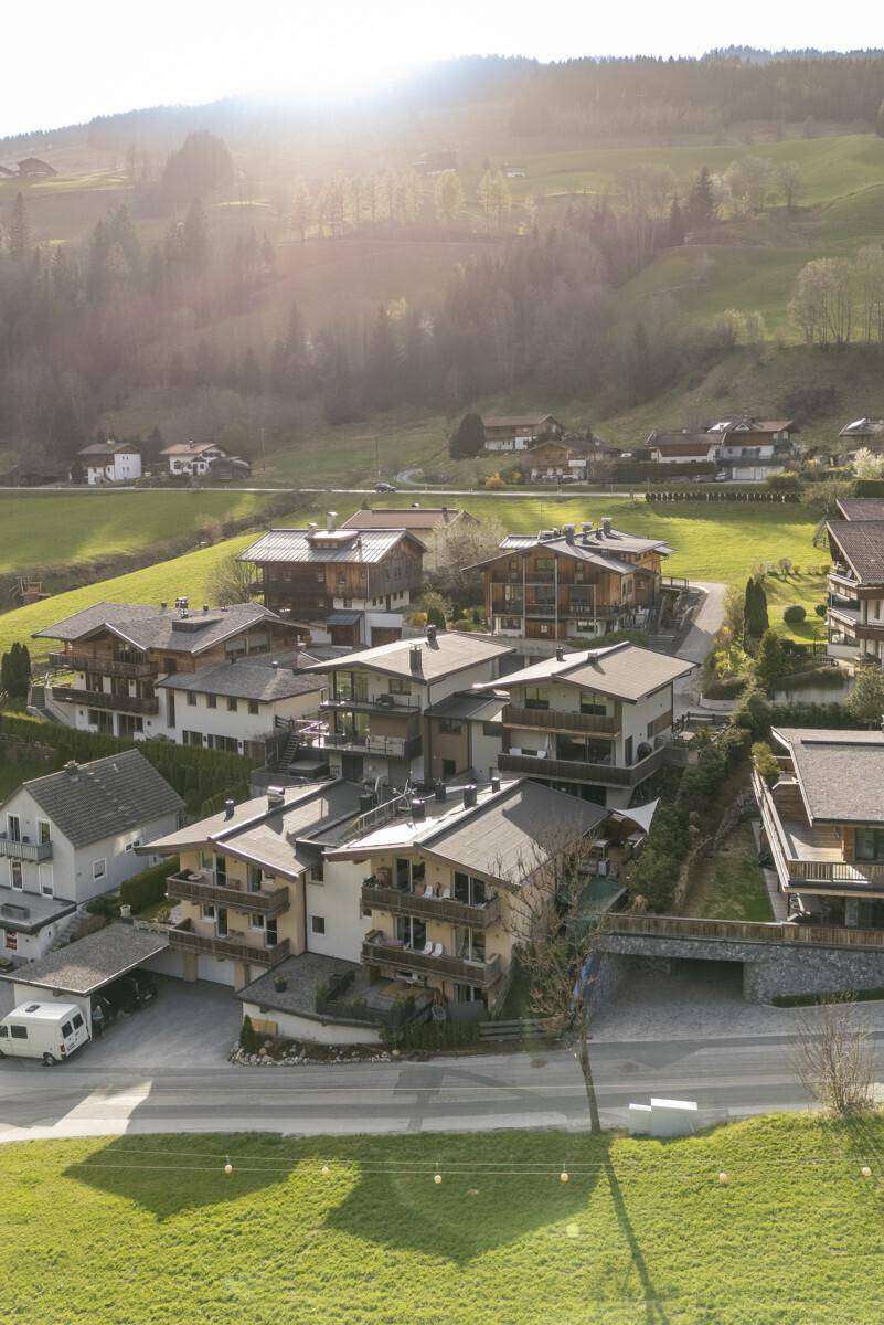 Luftaufnahme eines Wohngebiets mit Häusern im alpinen Stil in einer sonnigen Berglandschaft.