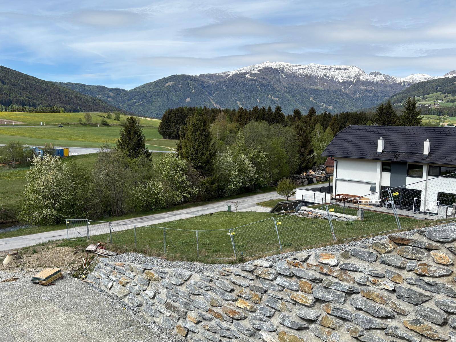 Haus in ländlicher Umgebung mit Blick auf schneebedeckte Berge und grüne Wiesen.
