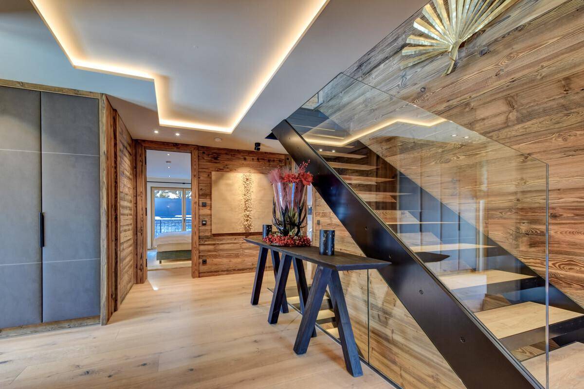 Heller Eingangsbereich mit moderner Treppe, Glasgeländer und Holzverkleidung.
