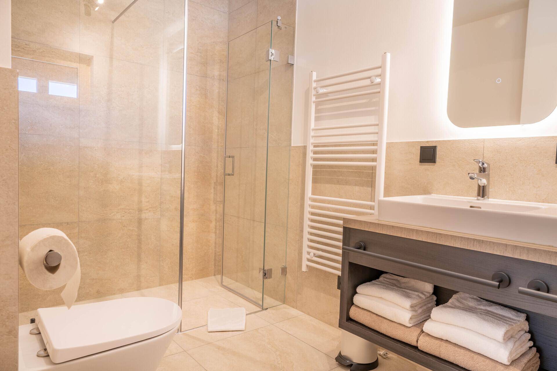 Modernes Badezimmer mit begehbarer Dusche, beigen Fliesen und beheiztem Handtuchhalter.